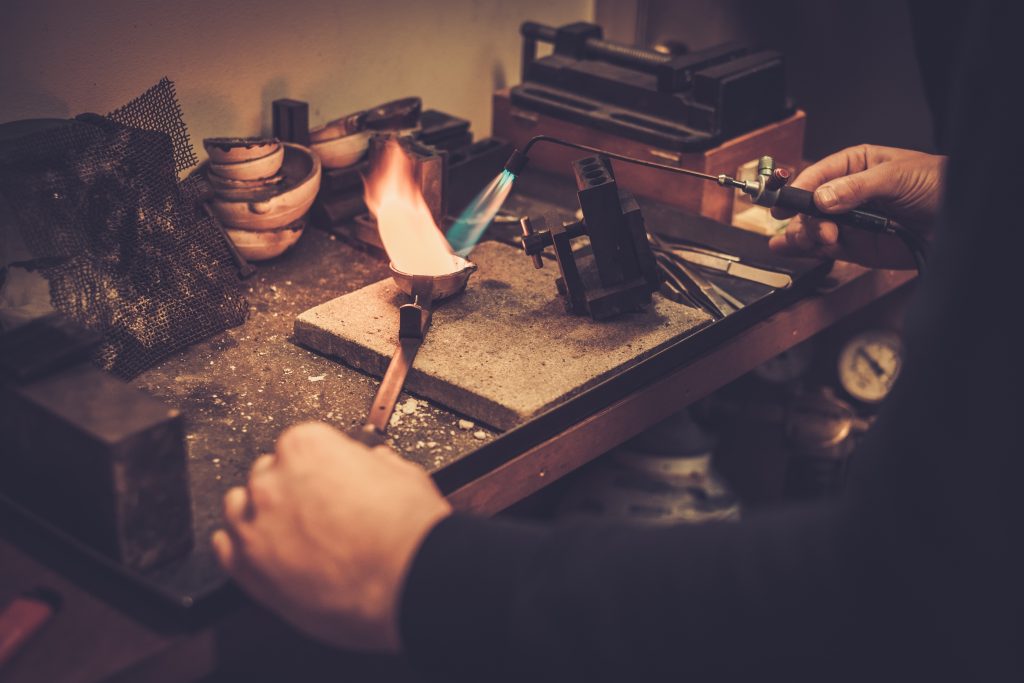 Goldsmith melting gold to liquid state in crucible with gasoline burner.