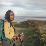 African American woman wearing a backpack while walking a hiking trail and carrying hiking poles with a perturbed facial expression. group communication and unspoken expectations
