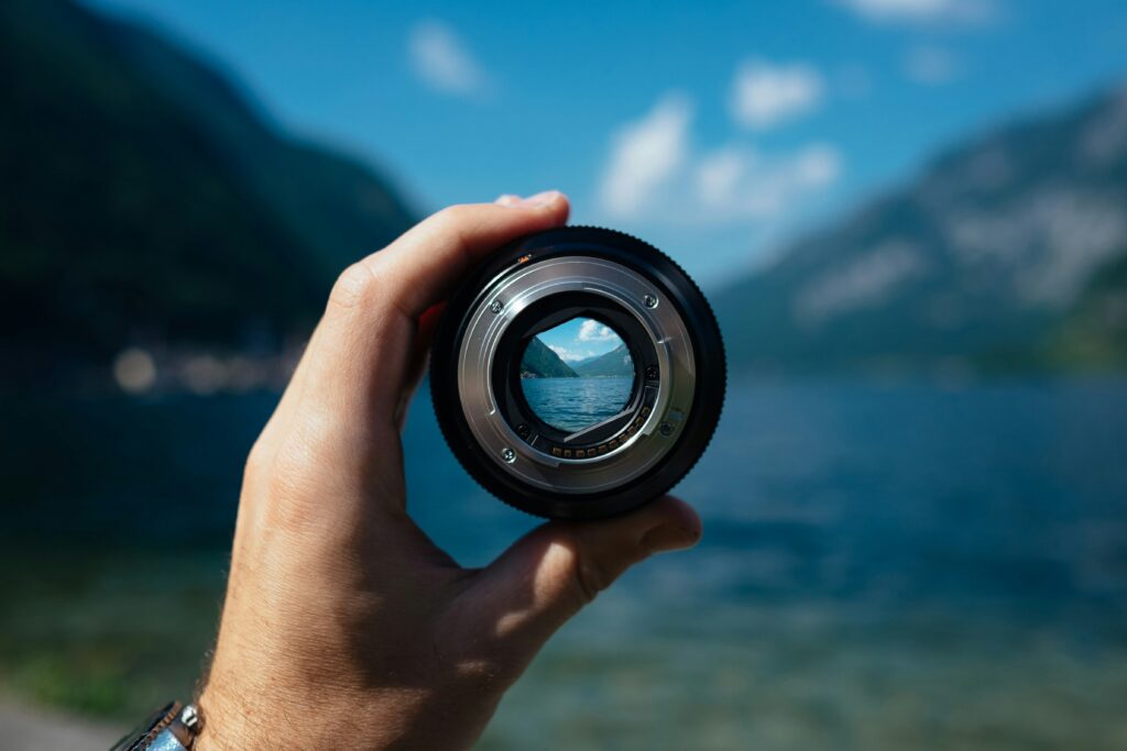 Camera lens held up to a mountain landscape — creating conditions for change starts with clarity of vision