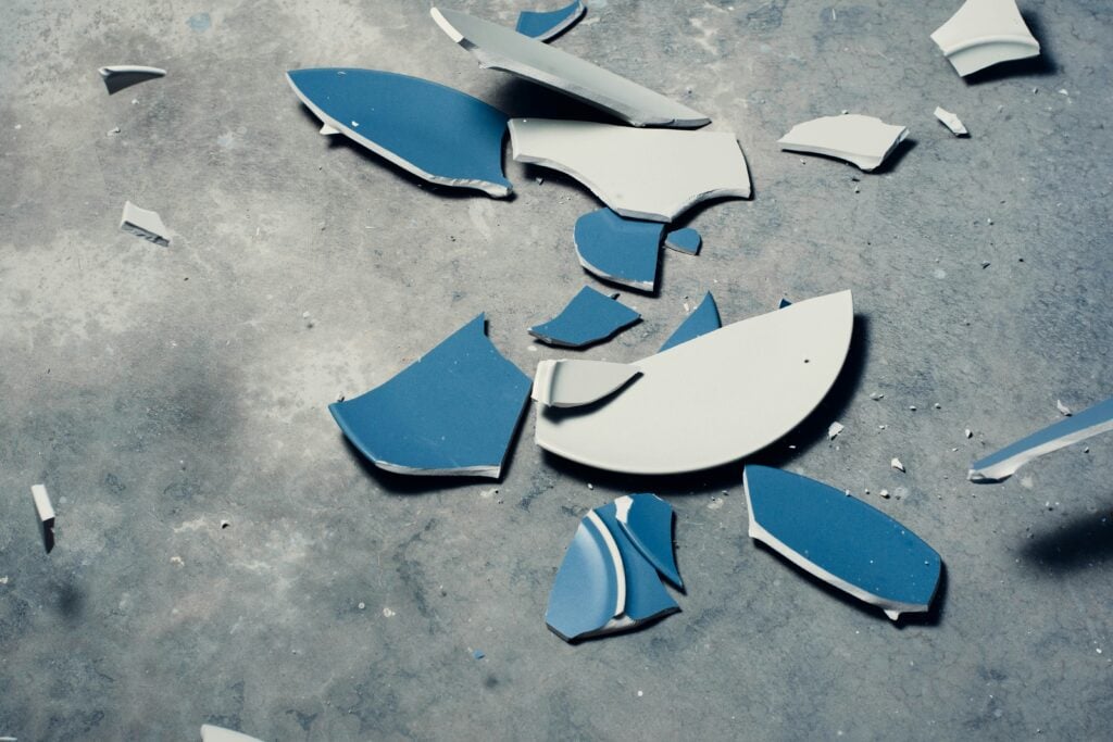 Broken blue and white ceramic plate scattered on concrete floor, symbolizing broken trust in leadership development opportunities